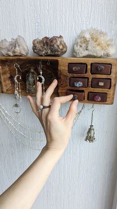 a person's hand is reaching for some jewelry on a wooden rack that holds several different types of rings and necklaces