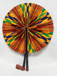 an orange and green decorative paper fan on a white background with brown leather shoes next to it