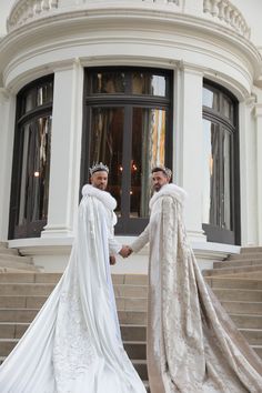 two men dressed in white are shaking hands on the steps outside an ornate building with large windows