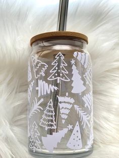 a clear glass jar with white christmas trees and snowflakes on it, sitting on a furry surface