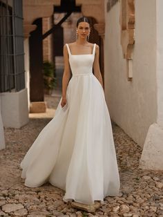 a woman in a white wedding dress walking down a cobblestone street with her hand on her hip