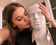 a woman kissing a mannequin's head in front of a white dummy