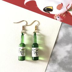 a pair of green bottle earrings sitting on top of a piece of paper next to a stuffed animal