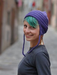 a woman with green hair wearing a purple knitted hat on her head and smiling at the camera