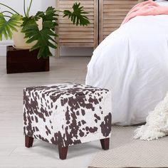 a cow print foot stool sits in front of a bed