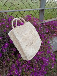 a crocheted bag sitting on the ground next to purple flowers