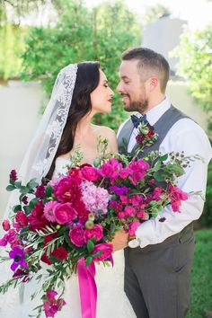 the bride and groom are posing for a wedding photo with pink flowers in their bouquets