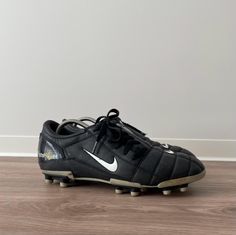 a pair of black and white nike soccer cleats on wooden floor next to wall