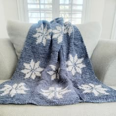 a blue and white crocheted blanket sitting on top of a couch next to a window