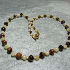 This necklace is made from Tigers Eye gemstone beads, in three sizes, alternate with 2 sizes of yellow Jasper separated by gold coloured glass seed beads. The Tigers Eye gemstones are 4mm at each end of the necklace changing to 6mm then 8mm at the centre, while the Jasper is 4mm at each end changing to 6mm. The magnetic clasp is gold plated stainless steel and the necklace comes with free matching earrings all enclosed within a cream fine velvet bag. Yellow Spiritual Beaded Necklace With Gemstone Beads, Spiritual Gold Beads Gems And Cabochons With Natural Stones, Gold Spiritual Gemstone Beads, Spiritual Brown Necklace With Spacer Beads, Gold Spiritual Crystal Necklace With Polished Beads, Gold Spiritual Beaded Necklaces With Gemstone Beads, Gold Beaded Necklaces With Gemstone Beads For Spiritual Style, Yellow Necklaces With Natural Stones And Round Beads, Gold Spiritual Beaded Necklace With Gemstone Beads