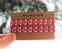 two red and white braided hair ties in front of a brown card with the words too much knots on it