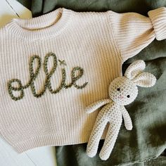 a knitted sweater with the word eile on it next to a stuffed bunny