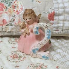 a little angel figurine sitting on top of a bed next to a teddy bear