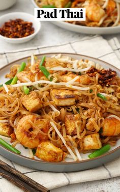 pad thai noodles with shrimp and scallops on a plate next to chopsticks