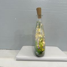 a glass bottle filled with green plants on top of a white countertop next to a wall