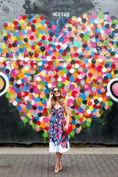 a woman standing in front of a wall covered with colorful circles and dots, talking on her cell phone