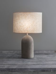 a gray table lamp with a white shade on the base and a wooden surface behind it