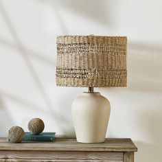 a white vase sitting on top of a wooden table next to a lamp and book