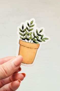 a hand holding up a sticker with a potted plant on it's side