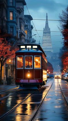 a red trolley car traveling down a street next to tall buildings in the background at night