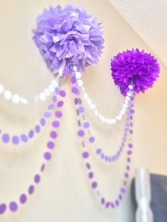 two purple pom - poms hanging from the side of a wall with beads