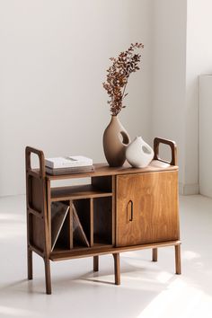 a table with a vase and some books on it next to a book shelf that has a plant in it