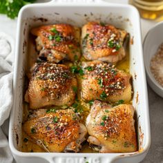 baked chicken thighs in a white casserole dish with herbs and seasoning on top