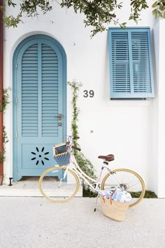 a bicycle parked in front of a blue door and shutters on a white building