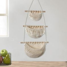 three macrame baskets hanging on a wall next to an apple in a basket