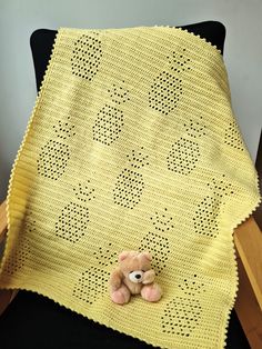 a teddy bear sitting on top of a yellow crocheted blanket next to a black chair