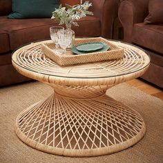 a wicker table topped with a glass vase filled with flowers on top of a rug