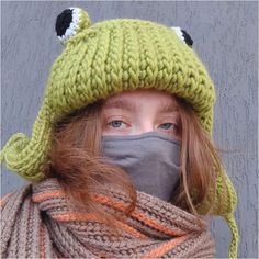 a woman wearing a knitted hat and scarf with a frog face on the front