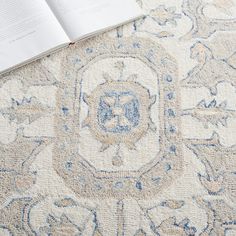 an open book sitting on top of a carpet covered in blue and white designs,