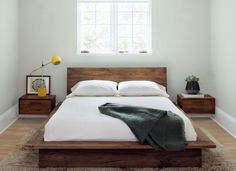 a bed with white sheets and pillows in a bedroom next to two nightstands on either side of the bed