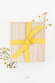 a wooden box with a yellow ribbon tied around it and flowers in front of it