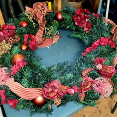 a christmas wreath with red and gold ornaments on it, sitting on a table next to a pair of scissors