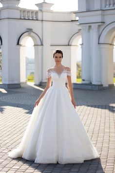 a woman in a white wedding dress standing on a brick walkway with an archway behind her