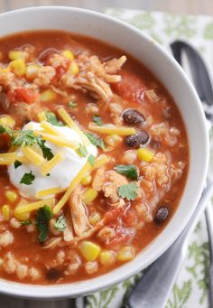 a white bowl filled with chili, beans and sour cream on top of a green napkin