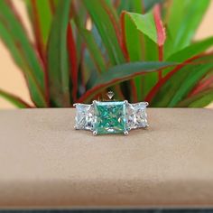 three stone ring sitting on top of a table next to green plants and red leaves