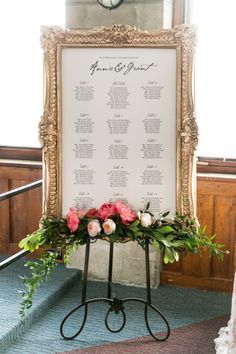 a wedding seating chart with flowers and greenery in front of a gold framed frame