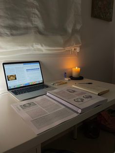 an open laptop computer sitting on top of a desk next to a book and candle