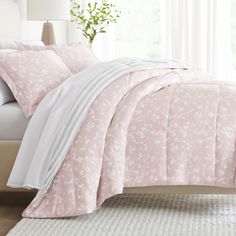 a bed with pink comforter and white sheets in a room next to a window