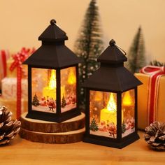 two small black lanterns sitting on top of a wooden table next to christmas presents and pine cones