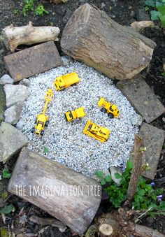 some yellow toy cars sitting on top of a pile of rocks and gravel in the middle of a garden