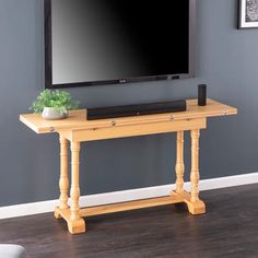 a flat screen tv sitting on top of a wooden table in front of a gray wall