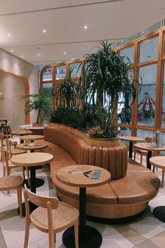 an indoor seating area with round tables and plants on the wall behind it, in front of large windows