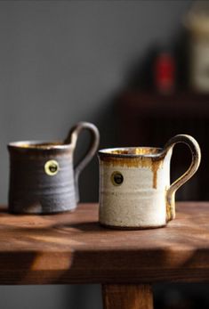 two coffee mugs sitting on top of a wooden table next to eachother