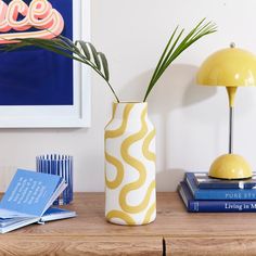 a vase with some plants in it sitting on a table next to books and a lamp