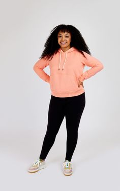 a woman in an orange hoodie and black pants poses for the camera with her hands on her hips