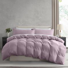 a bed with pink comforter and pillows in a room next to a lamp on a table